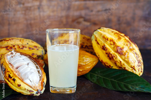 Fresh cacao water in glass and half sliced ripe yellow cacao pod with white cocoa seed, Cacao juice in glass  on vintage wooden background