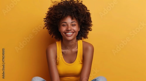 Happy young african american woman with curly hair toothy smiling at camera against yellow background photo