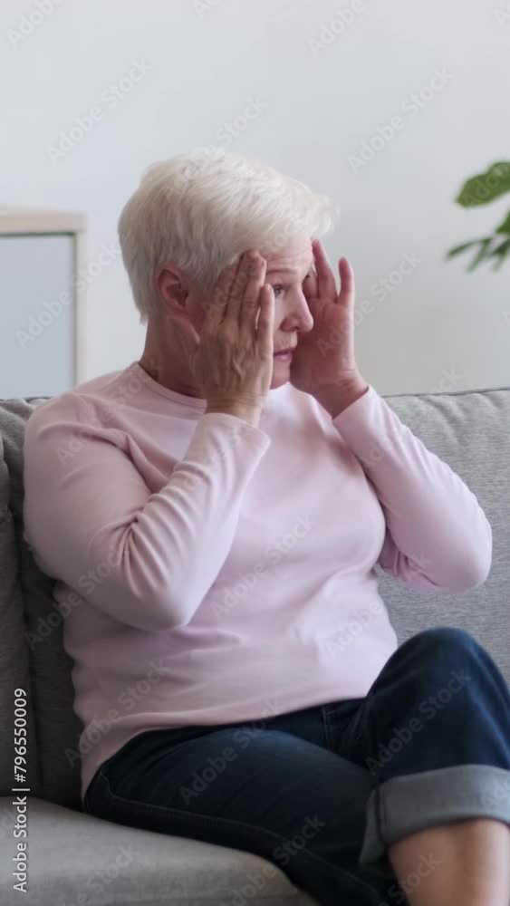 Unhealthy Caucasian senior adult woman with headache, sitting on sofa at home. Illness, annoyance, exhaustion concept. Vertical video. Unhealthy Caucasian senior adult woman with headache, sitting on sofa at home. Illness, annoyance, exhaustion concept. Vertical video.