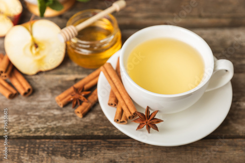 Fototapeta Naklejka Na Ścianę i Meble -  Fragrant hot tea with cinnamon stick and anise on a textured wooden background. A cup of hot tea with honey, lemon, mint and apples. Spicy tea with spices. Immunity tea. Health concept.Copy space.