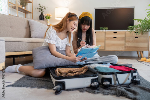 Young Asian woman packing clothes to the suitcase. Preparation for the summertime vacation. Two women are planning a trip and helping to prepare luggage to travel