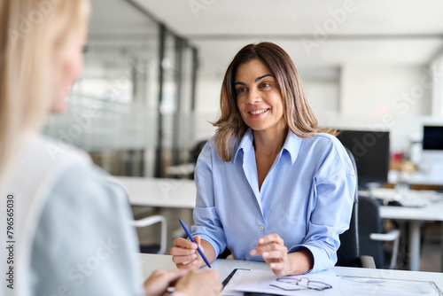 Happy middle aged business woman hr talking to recruit at job interview meeting. Smiling mature female financial advisor, professional bank manager consulting client working in corporate office.