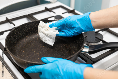 a hand in a rubber glove wipes a frying pan with a paper towel.