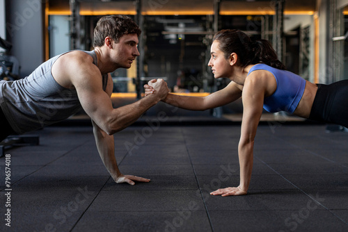 Fit sportive man and woman doing plank core exercise in the gym, and standing on one hand, giving high five to each other, side view