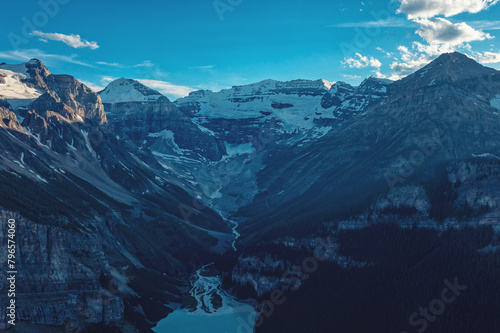 Drone view of winding frozen river flowing from mountains. Landscape of snow mountain peaks. Canada.