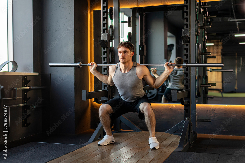 Strong sportsman squat with barbell in gym, young strong guy do exercises, have muscular body Strong sportsman squat with barbell in gym, young strong guy do exercises, have muscular body