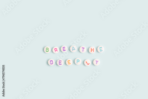 Breathe deeply. Quote made of white round beads with multicolored letters on a blue background.