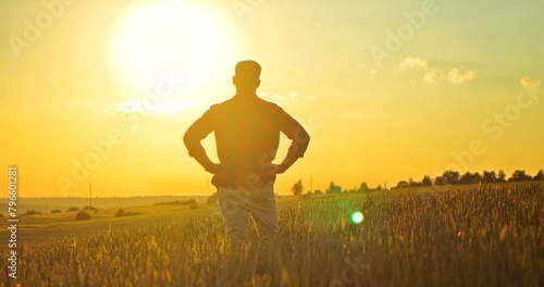 Back view of man farmer looking at the field and analyzing harvest while standing with sunset at the background. Agricultural concept