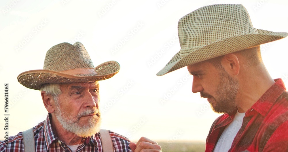Fototapeta premium Portrait view of the two farmer engineers wearing hat examining plants and controlling water system in the field while standing and discussing. Organic farm business concept