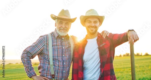 Great team. Waist up portrait view of the two male farmers wearing hat embracing and looking at the camera while working at the field. Farmer concept