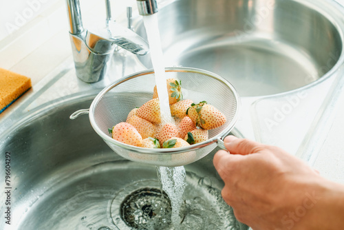 man rinses some white strawberries in a colander photo