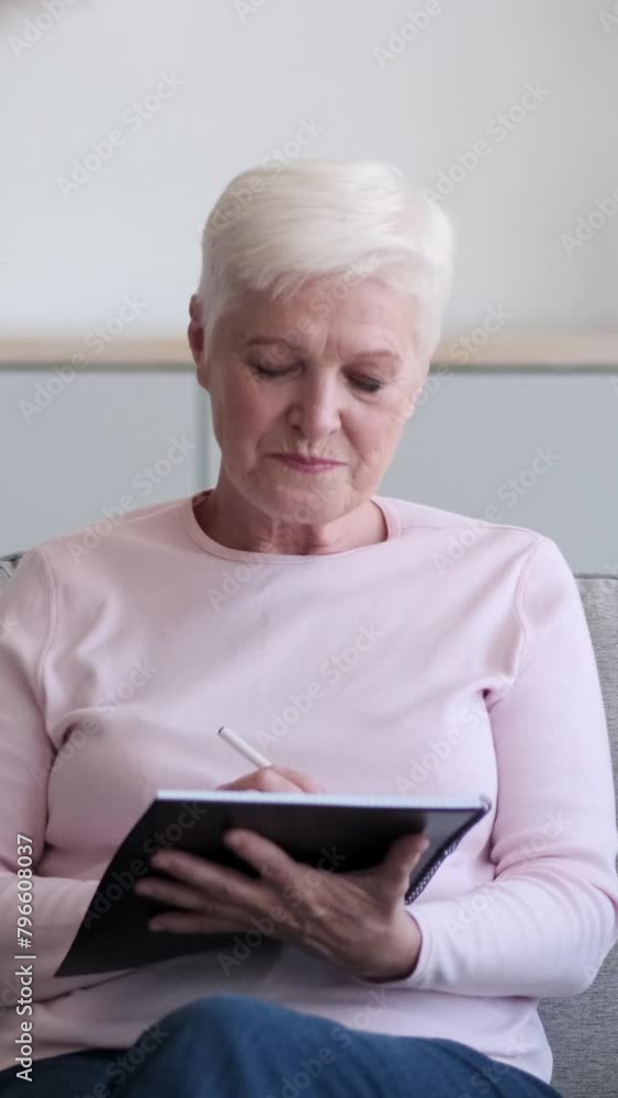 Happy senior Caucasian woman daydreaming and making notes, creating shopping list or planning agenda in notebook at home. Vertical video. Happy senior Caucasian woman daydreaming and making notes, creating shopping list or planning agenda in notebook at home. Vertical video.