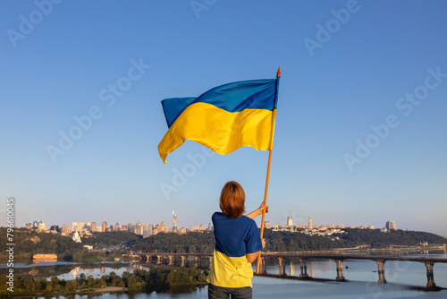 woman raises a large yellow-blue Ukrainian flag, standing high on a roof in Kyiv in front of the Dnieper river. Be proud that you are Ukrainian. Independence Day. faith in victory. stop the war