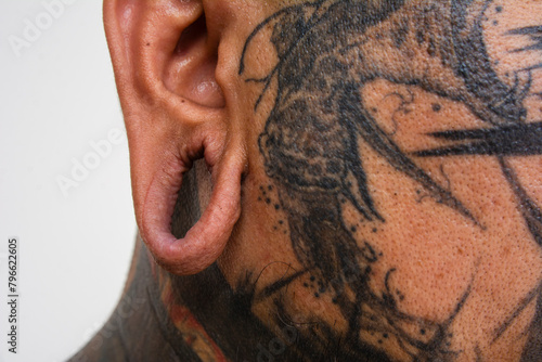 An stretched earlobe with the flesh tunnel removes, showing a stretched hole. Closeup of the ears of a man with extensive face tattoos. photo