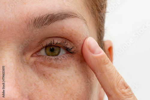 Close up cropped eye of middle aged caucasian woman looking at camera holding finger on eyelid photo