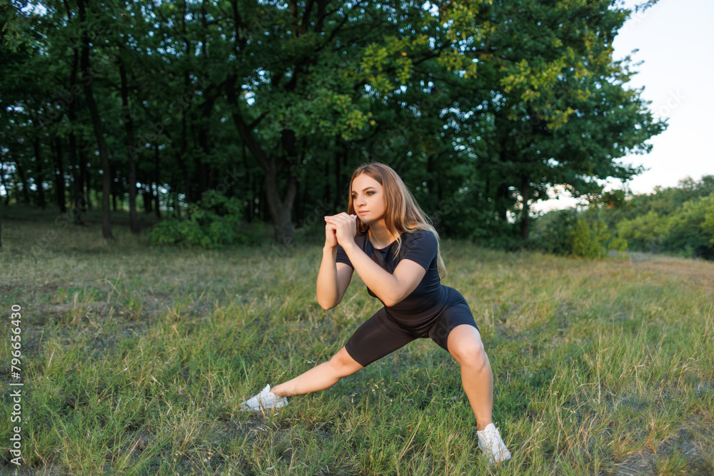 A girl in nature performs stretching of leg muscles. Athletic girl in a tight uniform working outdoors in the park. A girl in nature performs stretching of leg muscles. Athletic girl in a tight uniform working outdoors in the park.