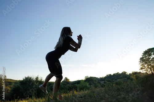 Silhouette of a girl against the background of sunset girl doing sports. Athletic girl in a tight uniform working outdoors in the park.