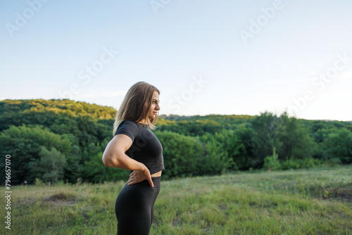 The athletic girl put her hands on her hips and stares off into the distance. Athletic girl in a tight uniform working outdoors in the park.