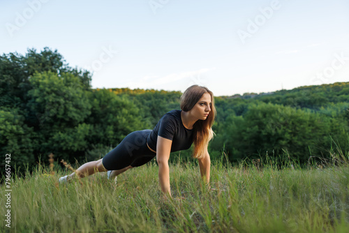 Athletic girl standing on her hands and trying to do push-ups. Athletic girl in a tight uniform working outdoors in the park.