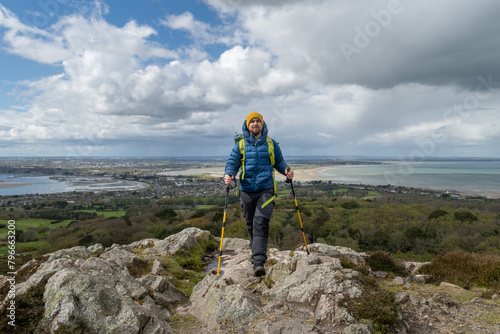 Hiker reaches the top of the mountain with hiking poles. © Simon