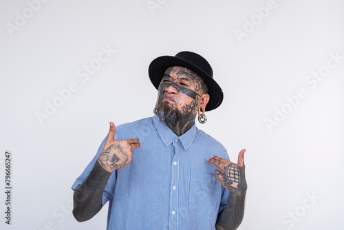 A confident, stylish Asian man covered in face tattoos and multiple piercings smugly points to himself against a clean white background. photo