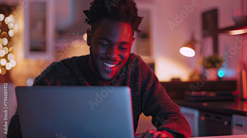 Young man using laptop and smiling at home. Man sitting by table working on laptop computer.