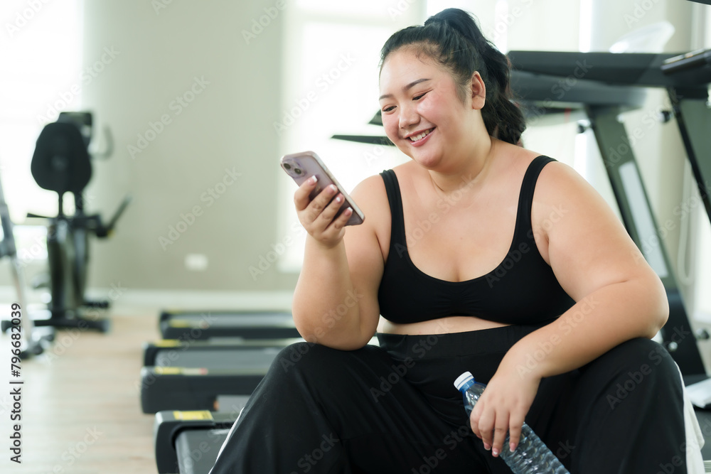 Chubby Asian woman exercise in gym, smiles while talking on phone, taking joyful break. With a beaming smile, a young fitness enthusiast enjoys conversation on her phone amidst workout session Chubby Asian woman exercise in gym, smiles while talking on phone, taking joyful break. With a beaming smile, a young fitness enthusiast enjoys conversation on her phone amidst workout session