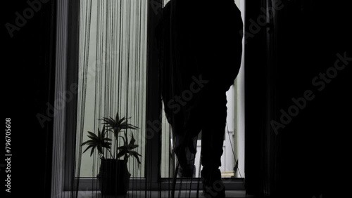 A thief or bandit in a mask breaks open a window with a crowbar and breaks into the house.