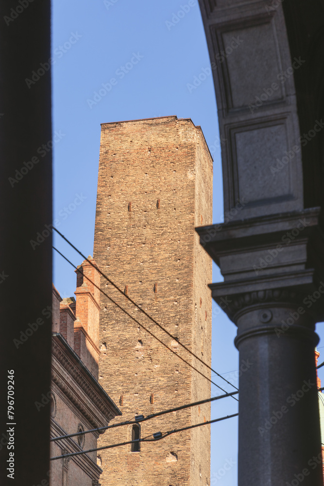 The iconic Asinelli Tower of Bologna peeks through an archway, its medieval brick structure standing tall against the blue Italian sky