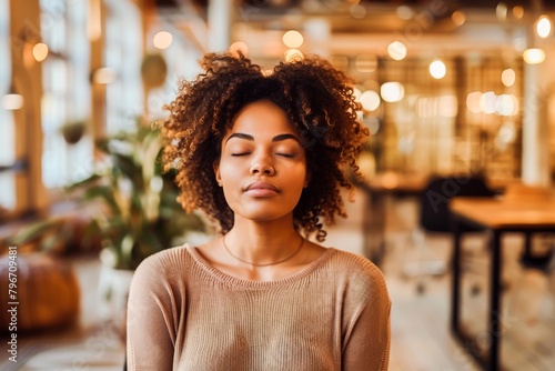 A peaceful young woman meditating with closed eyes, embracing tranquility and mindfulness in a modern office environment.