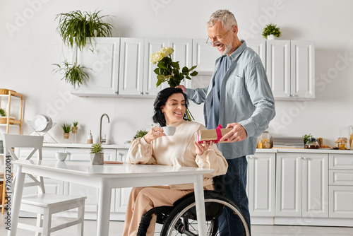 A man standing devotedly next to his disabled wife in a wheelchair in their kitchen at home. photo