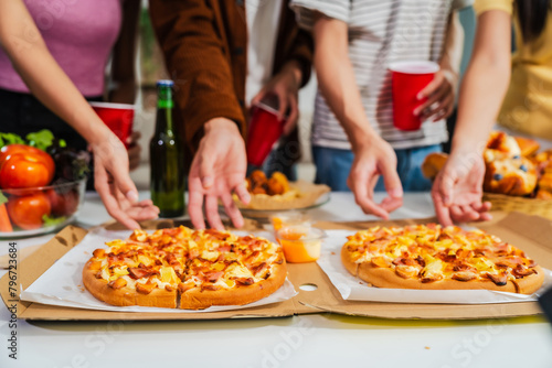 .Young Asian students gather with friends for a pizza party, laughing and sharing slices. Enjoying fast food delivery, they embody diversity and togetherness in a relaxed, enjoyable lifestyle. © NanSan