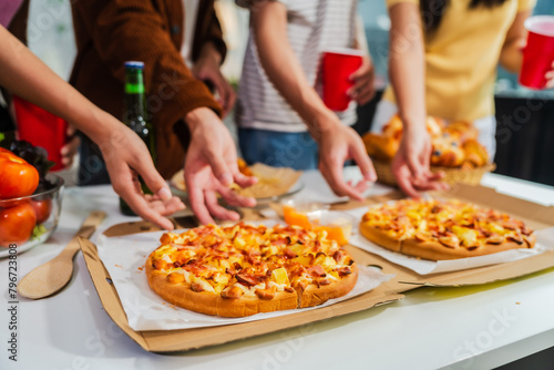 .Young Asian students gather with friends for a pizza party, laughing and sharing slices. Enjoying fast food delivery, they embody diversity and togetherness in a relaxed, enjoyable lifestyle.