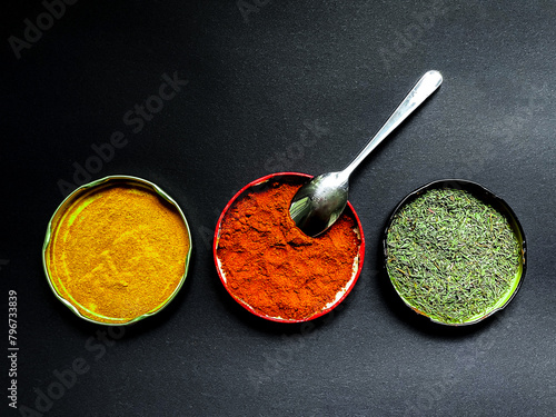 colorful spices with a spoon on black background © Monika