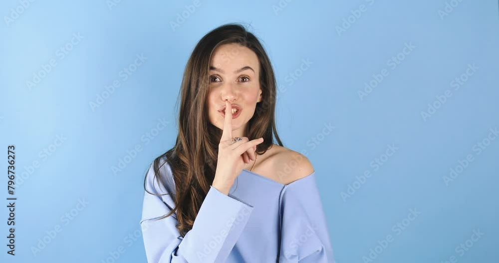 Happy brunette woman looking around by side and showing shh gesture in blue long sleeves standing isolated on blue background. Happy gossip girl, secret. Happy brunette woman looking around by side and showing shh gesture in blue long sleeves standing isolated on blue background. Happy gossip girl, secret.