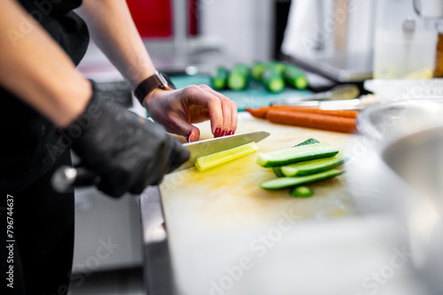 Person skillfully slicing cucumber on a cutting board in a kitchen, with carrots and other ingredients nearby, illustrating meal preparation