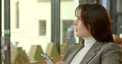 Businesswoman with smartphone twirling pen, clicking its cap in rhythmic motion. Action symbolizes intricate process of contemplation and decision making. Moment of reflection and consideration.