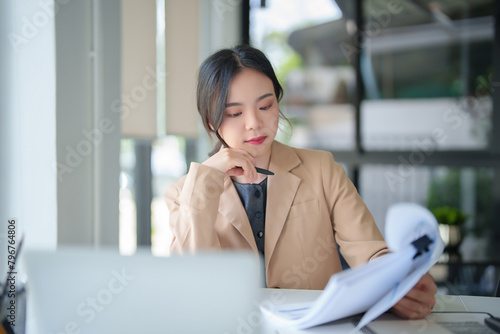 Businesswomen reading business document to thinking analysis strategy investment and management about new startup project while taking notes in paper and working with technology on digital laptop