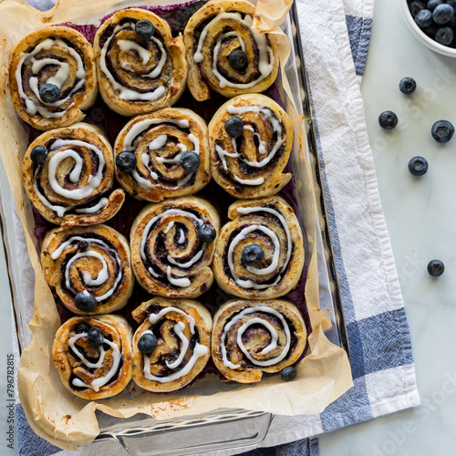 A dozen freshly baked blueberry cinnamon rolls, glazed with vanilla icing.