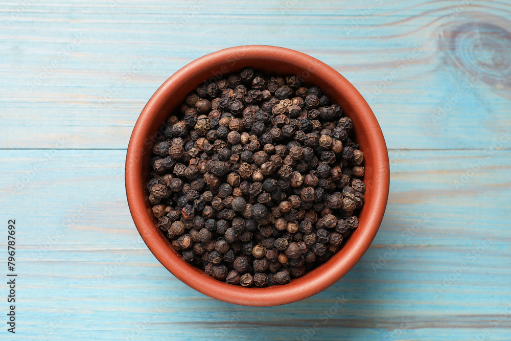 Aromatic spice. Black pepper in bowl on light blue wooden table, top view Aromatic spice. Black pepper in bowl on light blue wooden table, top view
