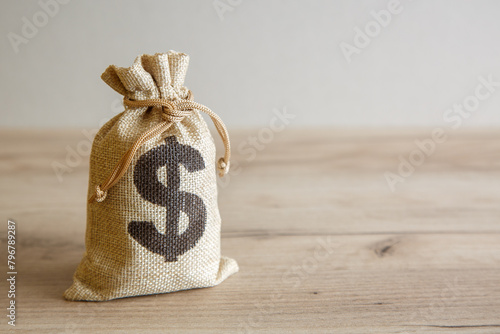 A bag with a dollar symbol on a wooden table. Space for text.