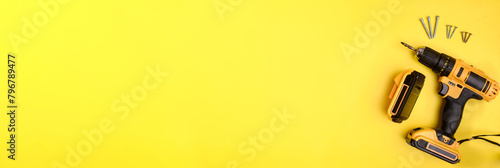 Banner: cordless electric yellow screwdriver, battery and screws on a yellow background. Copy space. Concept of construction, repair, electrical equipment. photo