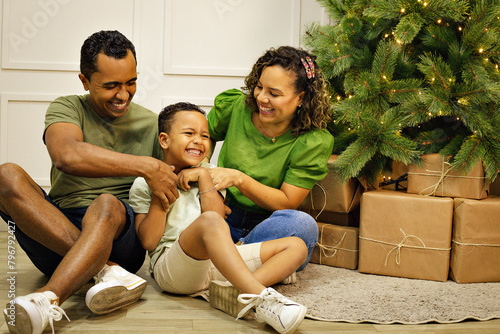 Familia Parda com traços brasileiros com homem, mulher e um menino criança, em uma sala com uma decoração de natal na cor verde. photo