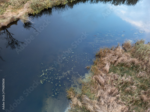 Aerial look down on river water surface with cloudy sky reflections and reeds on riverbanks