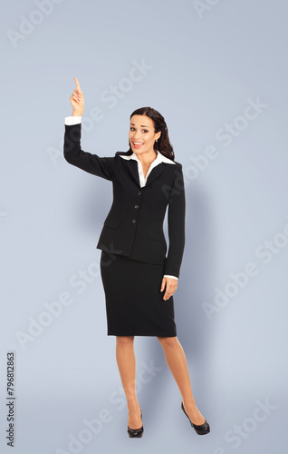 Full body happy, excited confident business woman, businesswoman showing pointing finger up advertise empty slogan text area. Isolated grey gray background. Ad concept image.