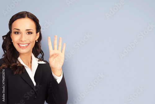 Ad concept image - happy smiling brunette businesswoman business woman executive person wear black confident suit, show four fingers hand sign gesture, isolated against grey gray wall background. © vgstudio