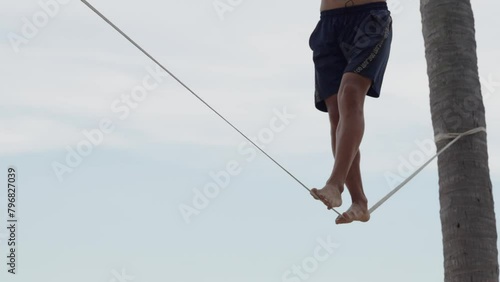 Male walking on the slack rope low angle view. Slack line tightened between palm trees. Healthy lifestyle concept.