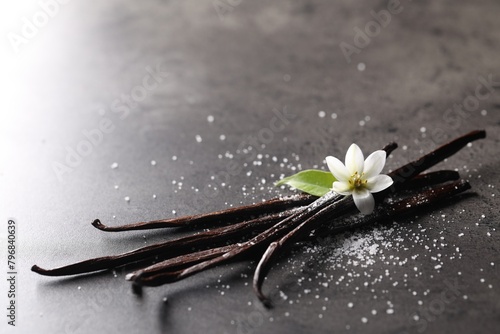 Vanilla pods, flower, leaf and sugar on grey textured table, closeup. Space for text