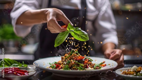 A chef garnishing a plate of Pad Kra Pao with fresh basil leaves and sliced chili peppers