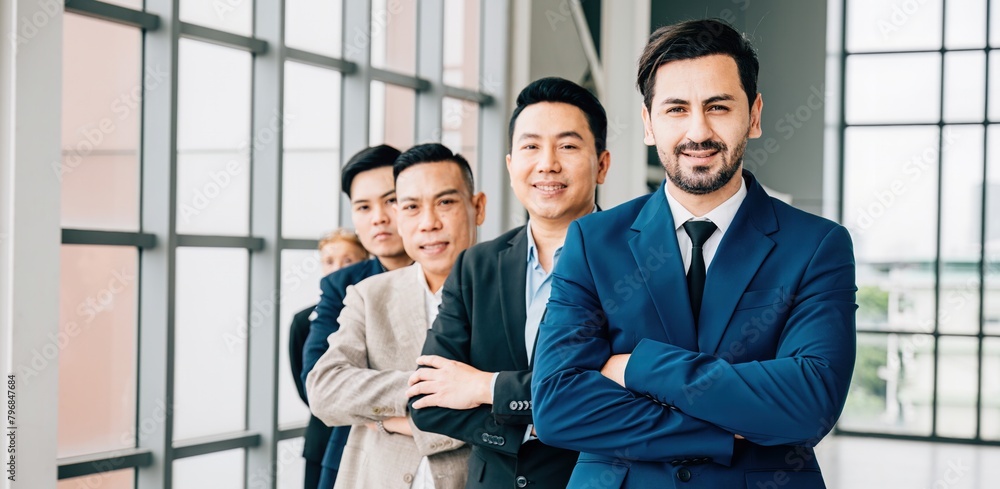 A united group portrait captures young businesspeople and a businessman confidently standing in the office with crossed arms. Their dedication to success and teamwork is evident. A united group portrait captures young businesspeople and a businessman confidently standing in the office with crossed arms. Their dedication to success and teamwork is evident.